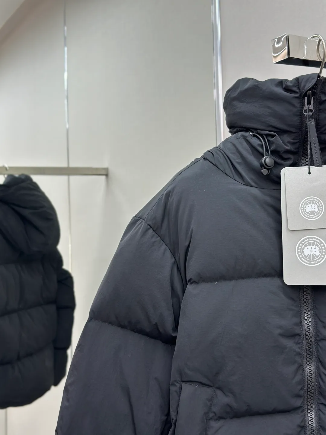 P1010 Canada Goose Black Label Badge Hooded Down Jacket (khaki) The high-quality filling is made of 90 national standard high-quality white duck down, selected high-loft velvet, weighing 240g, light and warm, with excellent temperature locking performance and good resilience. The fabric is woven with 400T high-count yarn. After special water-repellent treatment, the surface forms a lotus leaf effect - raindrops will slide down like beads, and snow particles will fall off when touched. The tear resistance reaches 200N (approximately 20kg load-bearing), the light gray matte texture breaks the stereotype of "outdoor clothing = hardcore", and the soft luster presents a high-end matte effect under urban neon lights, seamlessly switching scenes from ski resorts to CBD office buildings. The ribbon is woven with polyester as the base, and the brand letters are decorated on the ribbon through high-precision computer embroidery. The edges of the pattern are clear, the stitches are fine and even, and multiple layers of embroidery thread are stacked to enhance the three-dimensional effect. Precision thread reinforcement prevents linting and ensures the fluffy and resilient elasticity lasts as new. The embedded cuffs are three-dimensionally woven to form a "wavy" elastic structure, which forms natural folds when fitting the wrist, increasing the contact area with the skin, thus improving the windproof effect. At the same time, micro-velvet treatment is added to the inside of the cuffs, which feels like a second layer of skin and avoids friction on the skin from metal zippers or hard fabrics. Size:S-M-L-XL